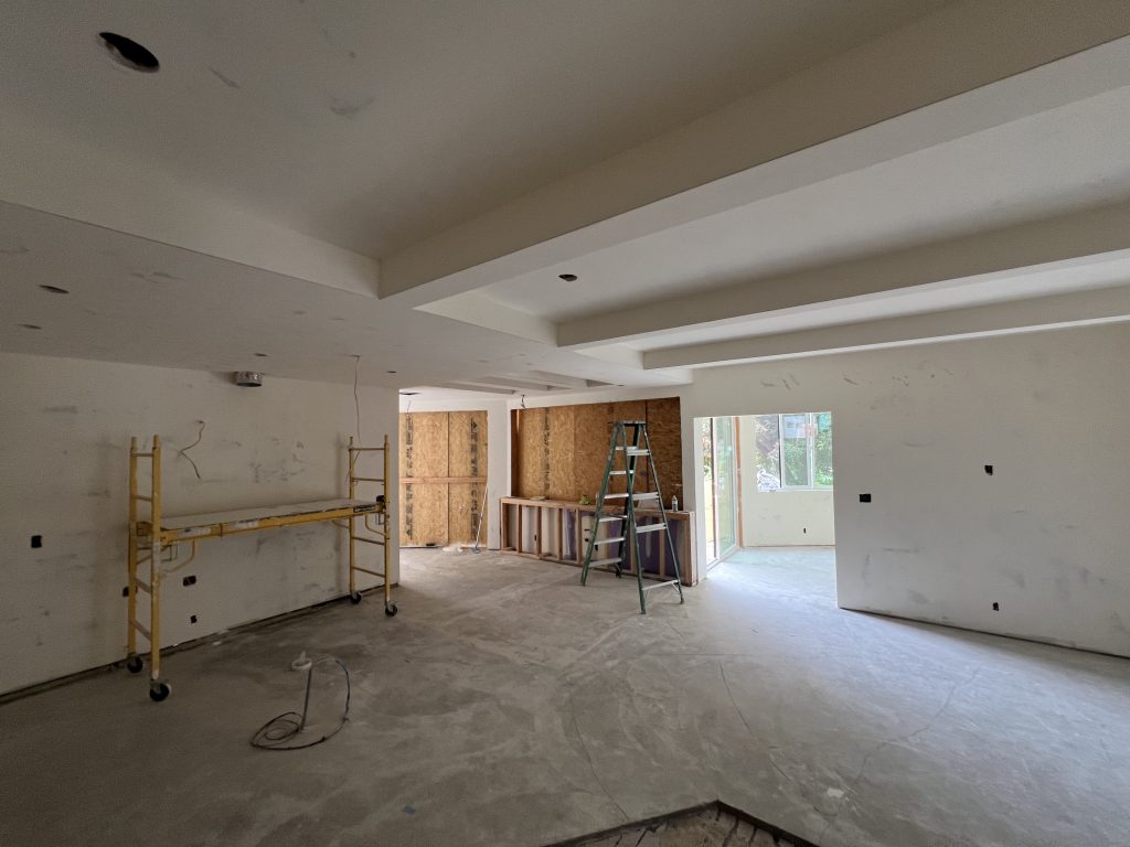 New drywall going up on the ceiling around beams during an open-plan remodel in Rancho Santa Fe